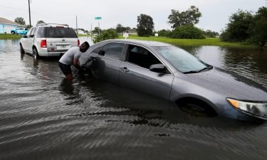 Cape Coral resident John Roberts helps tow a vehicle which became stuck as flooding made driving through the area too difficult on July 7.