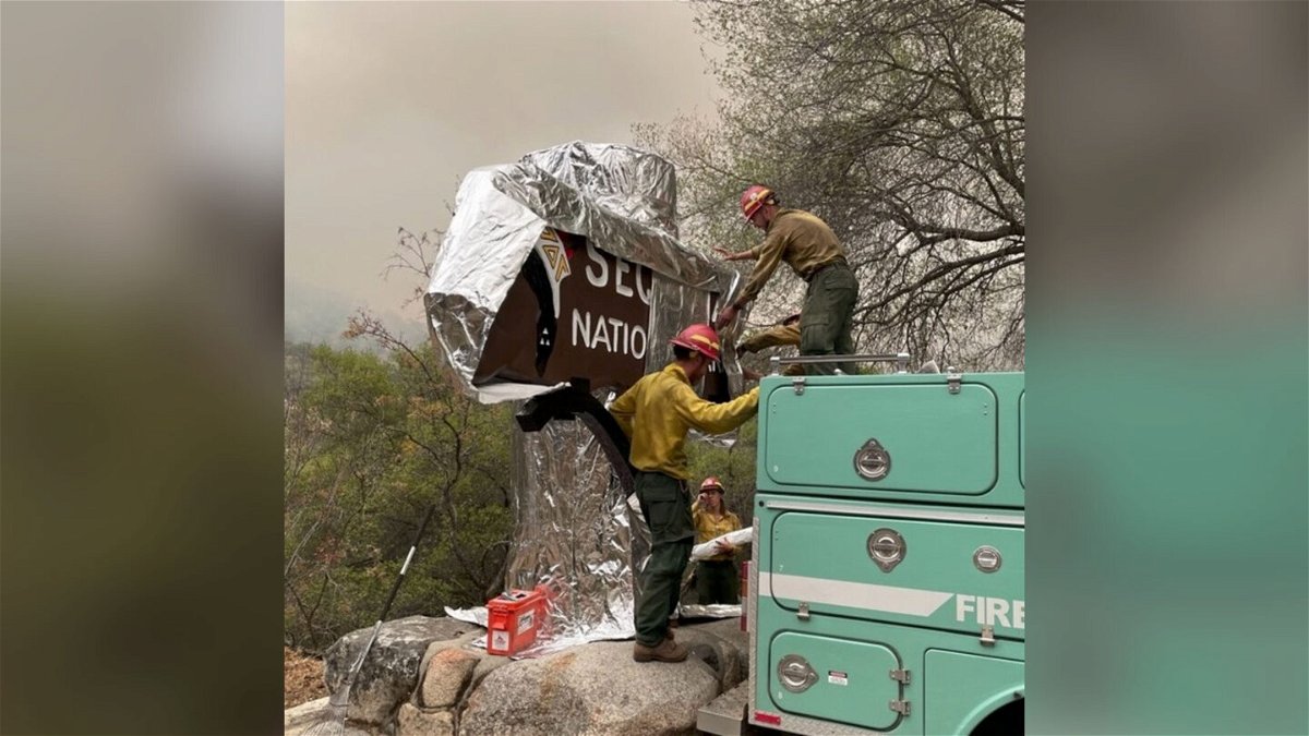 <i>From Sequoai & Kings Canyon National Parks/Instagram</i><br/>Firefighters assigned to the KNP Complex Fire prepare the historic Sequoia entrance sign for the possibility of fire in the area by wrapping it with aluminum-based burn-resistant material.