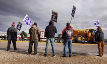 A truck hauls a piece of John Deere equipment from the factory past workers picketing outside of the John Deere Davenport Works facility on October 15 in Davenport
