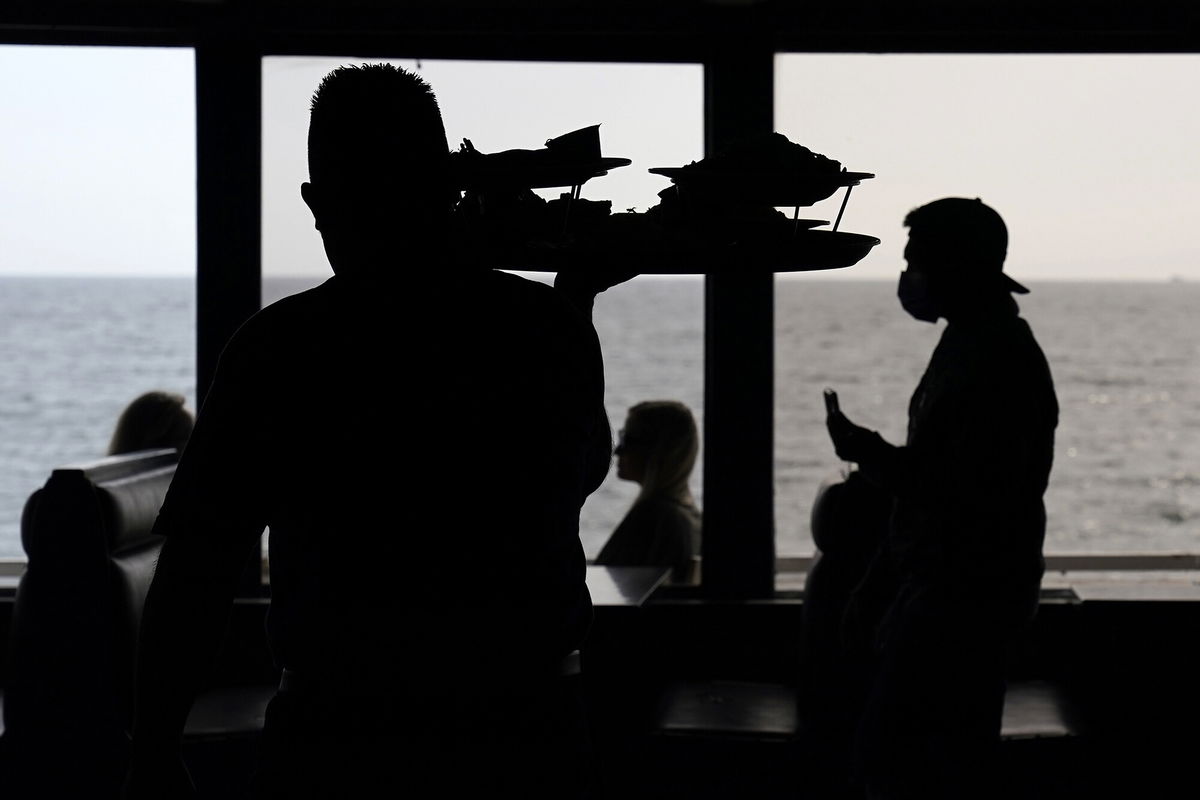 <i>Mark J. Terrill/AP</i><br/>Wait staff walk through a dining room as diners eat outside in front of beach views at a restaurant in Los Angeles in March 2021.