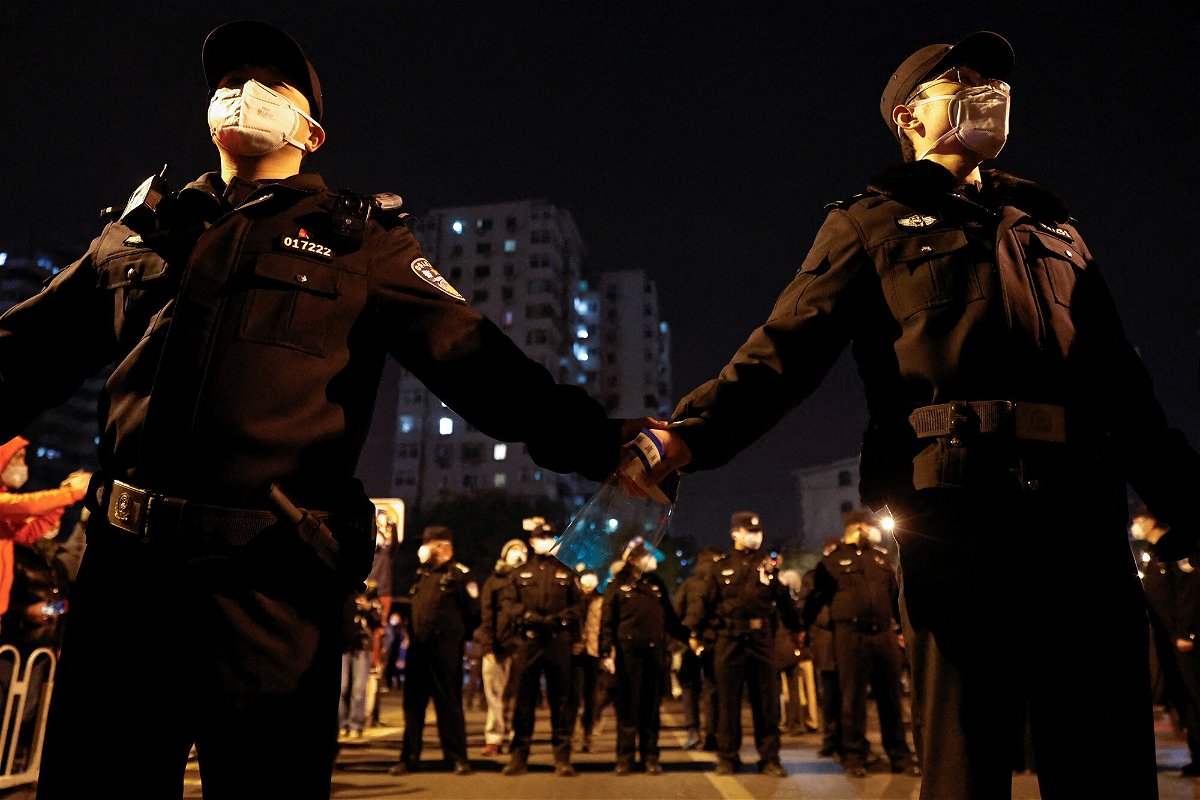 <i>Thomas Peter/Reuters</i><br/>Police officers stand guard as people protest coronavirus restrictions and hold a vigil to commemorate Urumqi fire victims