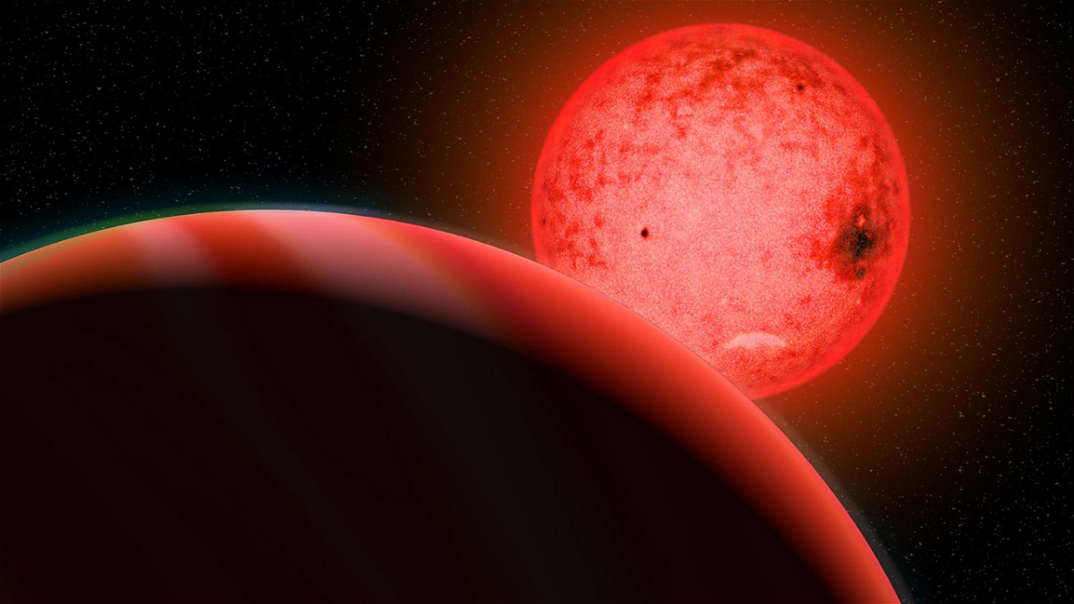 An artist's illustration shows a large gas giant planet (foreground) orbiting a small red dwarf star called TOI 5205.