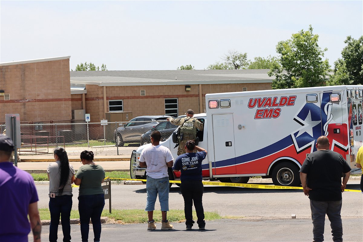 <i>Pete Luna/Uvalde Leader-News</i><br/>An ambulance waits at Robb Elementary School as people watch from behind police tape in Uvalde