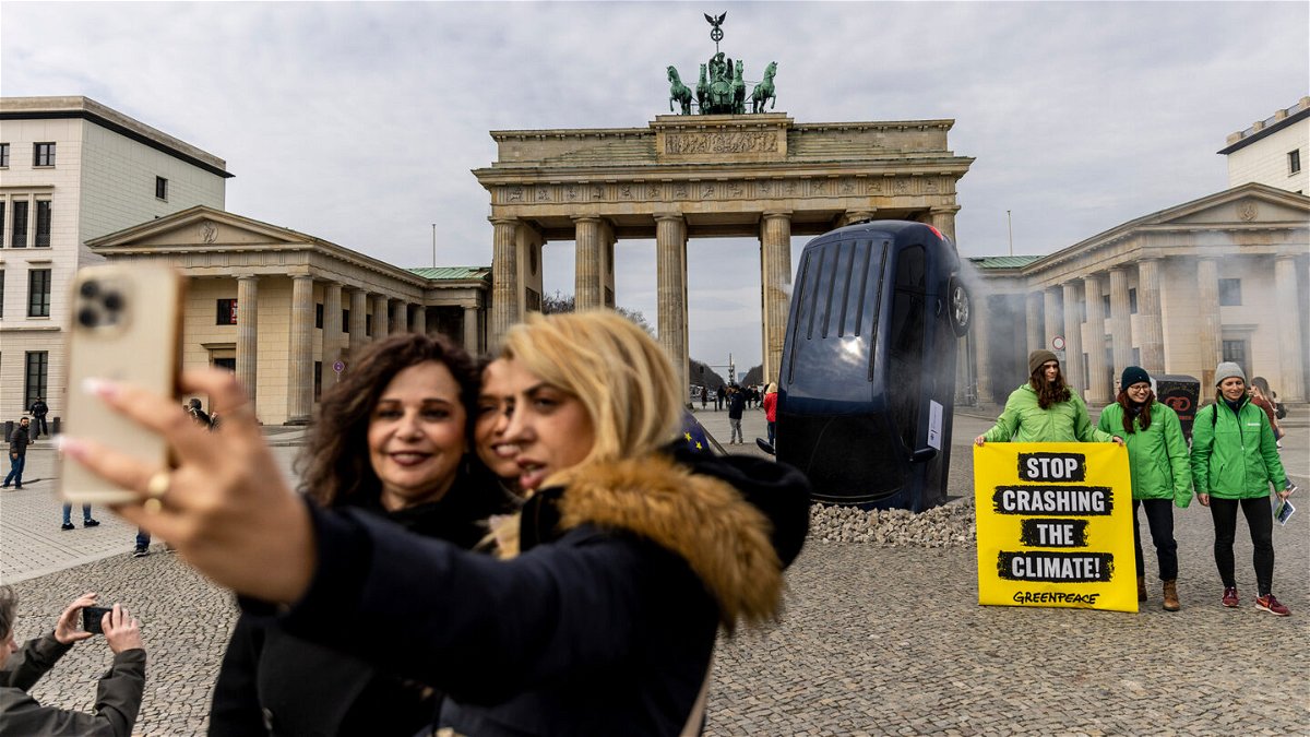 <i>Maja Hitij/Getty Images</i><br/>People take a selfie with an installation by Greenpeace activists showing an SUV that is seemingly rammed into the pavement in front of the Brandenburg Gate on March 22