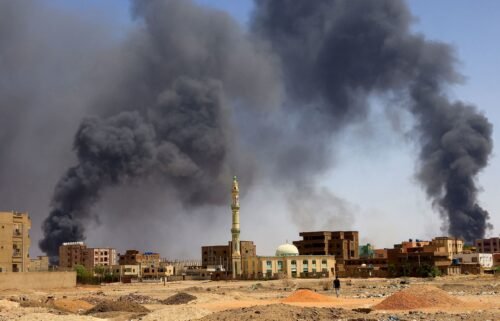 A man walks while smoke rises above buildings after aerial bombardment