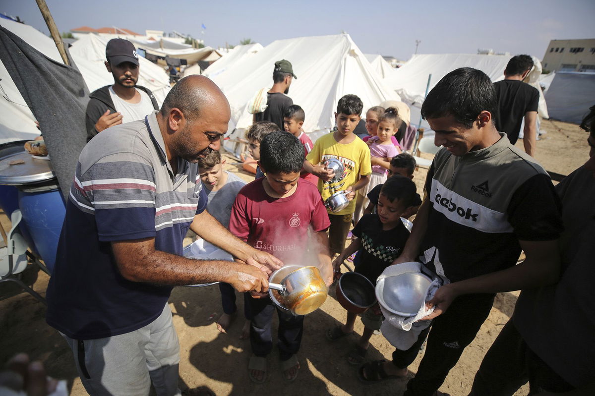 <i>Majdi Fathi/NurPhoto/AP</i><br/>Children receive food between tents set up for Palestinians seeking refuge on the grounds of a United Nations Relief and Works Agency for Palestine Refugees (UNRWA) center in Khan Yunis in the southern Gaza Strip amid the ongoing battles between Israel and Hamas.