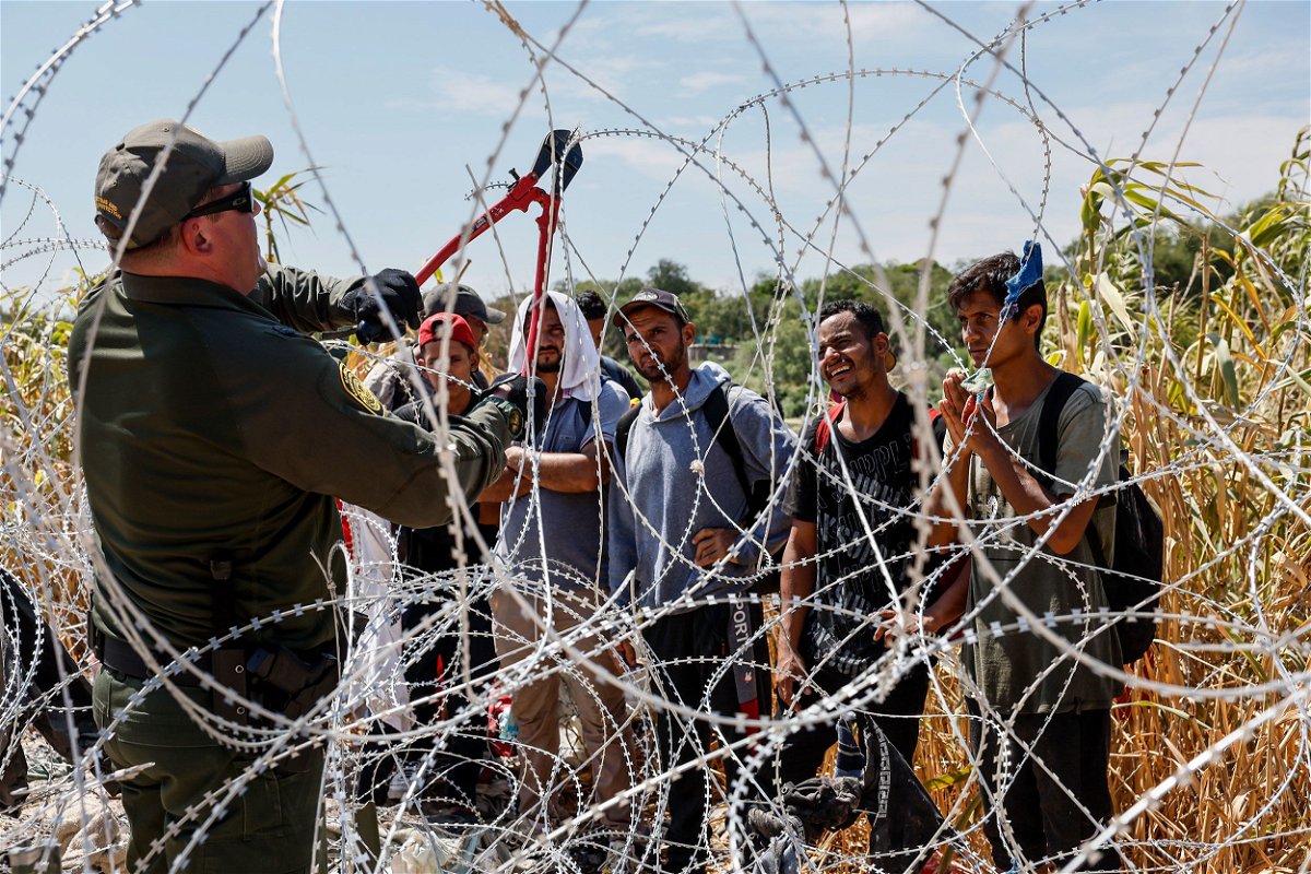 <i>Robert Gauthier/Los Angeles Times/Getty Images</i><br/>A border patrol agent cuts razor wire to allow migrants who've been waiting in the sun for hours