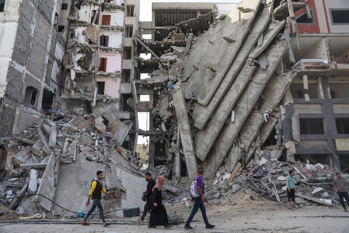 <i>Mohammed Hajjar/AP</i><br/>Palestinians walk through damaged buildings in Gaza City.