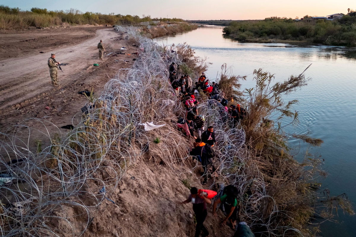 <i>John Moore/Getty Images</i><br/>Texas National Guardsmen watch as migrants pick their way through razor wire after crossing the Rio Grande into the United States on December 17 in Eagle Pass