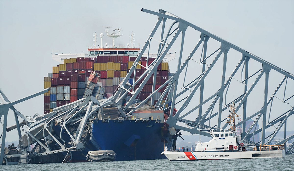 <i>Steve Helber/AP via CNN Newsource</i><br/>A Coast Guard cutter passes a cargo ship that is stuck under part of the structure of the Francis Scott Key Bridge after the ship hit the bridge Tuesday