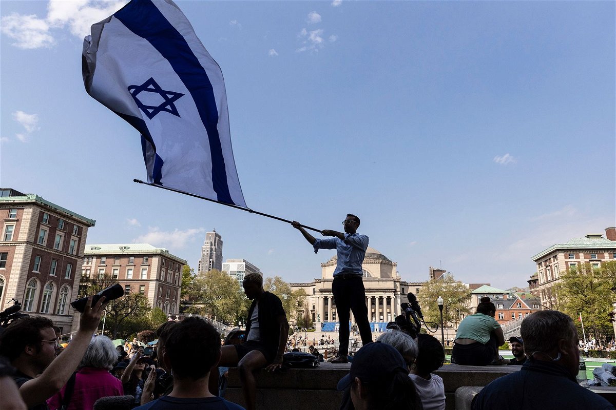 <i>Stefan Jeremiah/AP via CNN Newsource</i><br/>A student waves an Israeli flag outside the protest encampment on the Columbia University campus in New York City on April 29.