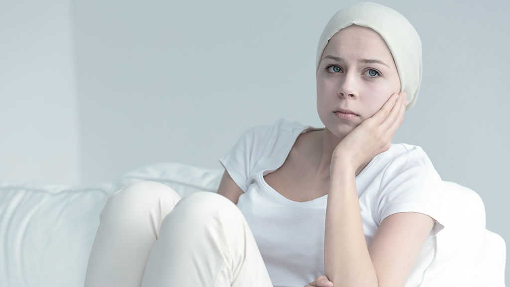 Woman with cancer sitting on a couch resting her hand against her cheek