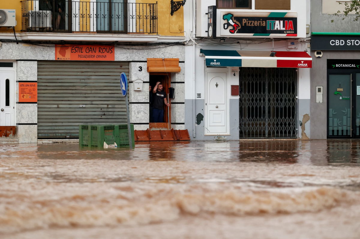 <i>Jorge Guerrero/AFP/Getty Images via CNN Newsource</i><br/>Men run next to a car covered with mud on a flooded street in Alora