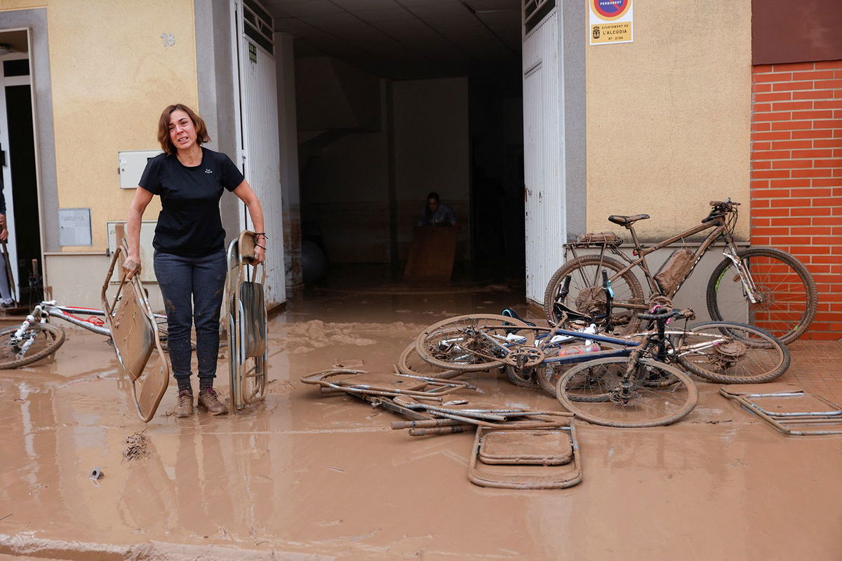 <i>Eva Manez/Reuters via CNN Newsource</i><br/>A woman carries chairs caked in mud after torrential rains caused flooding in La Alcudia