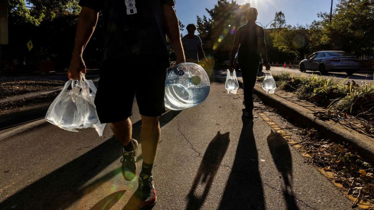 People walk with water collected from a truck in Asheville, North Carolina, on October 2, following Tropical Storm Helene. Eduardo Munoz/Reuters