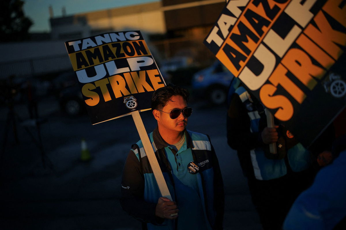 <i>Elijah Nouvelage/Reuters via CNN Newsource</i><br/>Amazon delivery trucks pass people holding signs and marching during a strike by Teamsters union members at an Amazon facility in Alpharetta