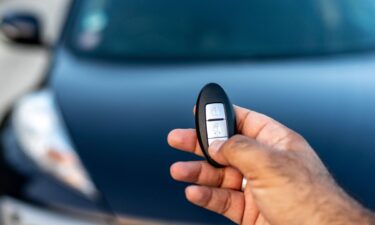 A person holding a keyless car remote in his hand by pressing the unlock button.