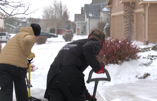 Two men shovel snow in a home's driveway.