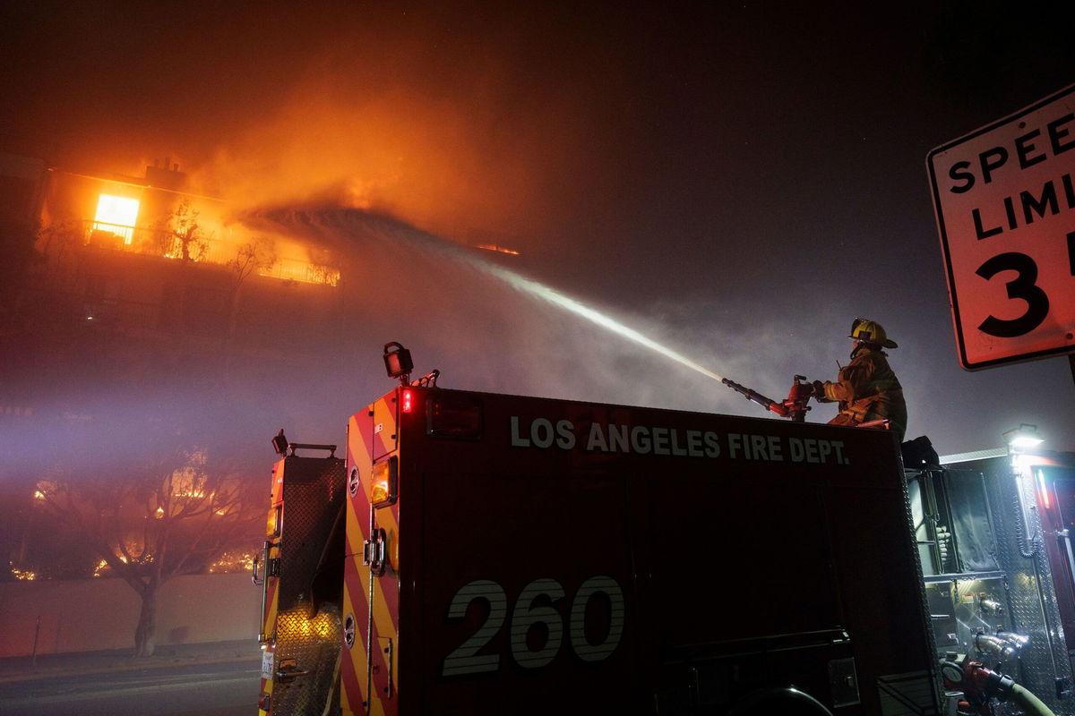 <i>Caylo Seals/SIPA USA/AP via CNN Newsource</i><br/>A Los Angeles Fire Department firefighter sprays water on a burning apartment complex caused by the rapidly spreading Palisades Fire in Los Angeles.