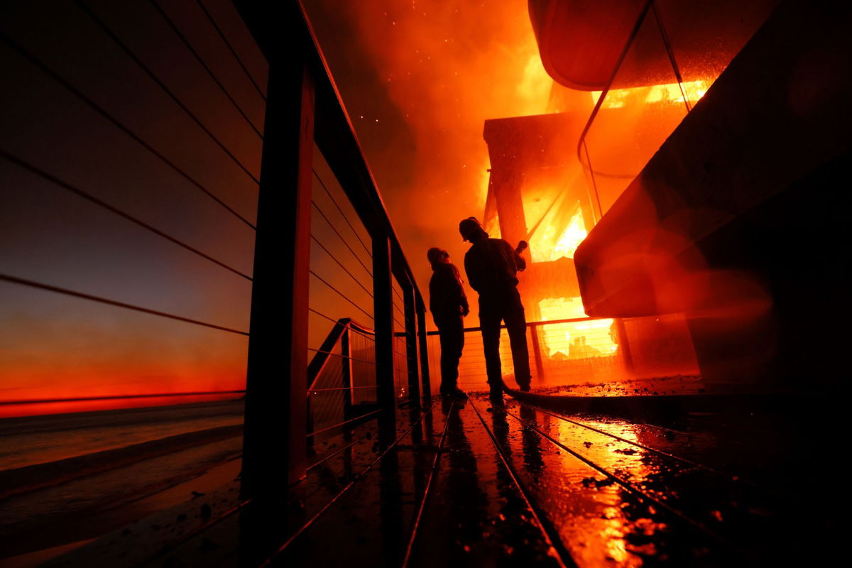 <i>Etienne Laurent/AP via CNN Newsource</i><br/>Firefighters work from a deck as the Palisades Fire burns a beachfront property in Malibu on Wednesday. The fires that have ravaged Los Angeles over the past week were larger and burned hotter than they would have in a world without planet-warming fossil fuel pollution.