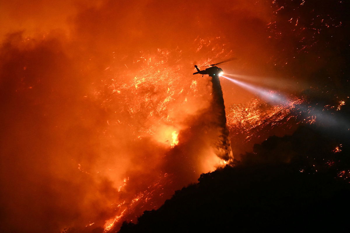 <i>Patrick T. Fallon/AFP/Getty Images via CNN Newsource</i><br/>A fire fighting helicopter drops water as the Palisades fire grows near the Mandeville Canyon neighborhood and Encino