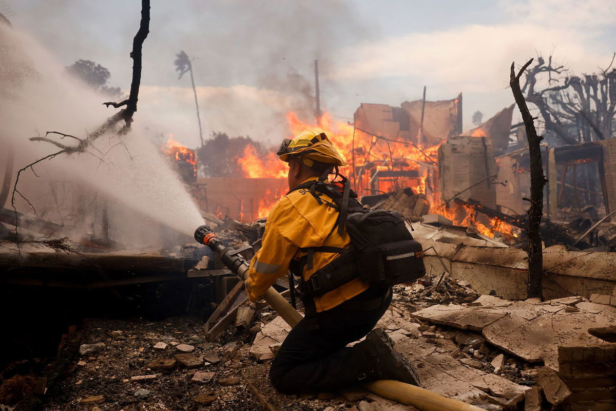 <i>Etienne Laurent/AP via CNN Newsource</i><br/>A firefighter battles the Palisades Fire around a burned structure in the Pacific Palisades neighborhood of Los Angeles on January 8.