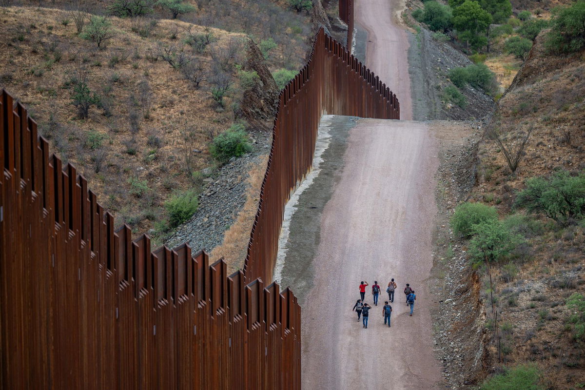 <i>Brandon Bell/Getty Images via CNN Newsource</i><br/>Migrants seeking asylum from Central and South America walk alongside border fencing after illegally crossing over into the U.S. on June 24